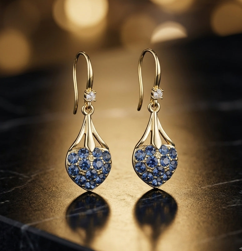 Blue crystal heart drop earrings gold tone on dark marble surface with bokeh lights